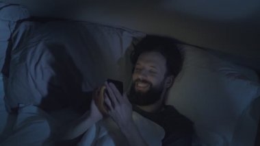 Gadget gecesi. Rahat adam yatakta telefonu kaydırıyor.