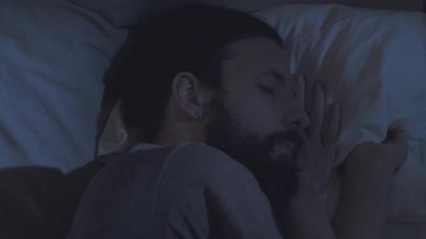 夜の休息のトラブルベッドに寝そべって疲れた男 — ストック動画