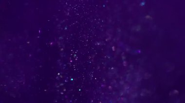 Parıltı dalgası. Odaklanamayan akış. Mor renkli mürekkep parlak sanat suyu akışını kaplıyor. Bulanık desen parlayan parçacıklar soyut arkaplanı harmanlıyor.