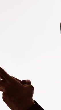 Dikey video. Karantina sohbeti. Uzaktan iletişim. Beyaz boş arkaplanda izole edilmiş telefon mesajı kullanarak yüz maskeli bir adamın karanlık profil silueti.