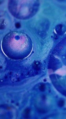 Dikey video. Köpük sıvısı. Odaklanmamış boya köpüğü. Parlak mavi pembe yağ dokusu soyut modern arka planda parıldayan sıvı.