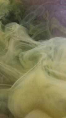 Dikey video. Duman sıçrıyor. Boya buharı. Odaklanamayan sarı mor renkli sis sıvı ruhani sis su akışı dumanı soyut sanat arka planında yükseliyor.