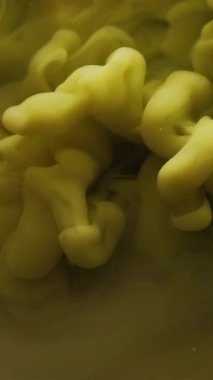 Dikey video. Boya damlası suyu. Duman bulutu. Odaklanmamış sarı renk buhar dokusu mürekkep sıvısı damlası soyut sanat arka planına yayılıyor..