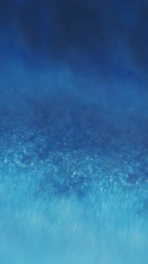 Dikey video. Mavi dalga. Odaklanamayan köpüklü su. Yanıp sönen yapışkan boya sıvısı bulanık bokeh ışığı üzerinde hareket ediyor soyut modern arka plan.