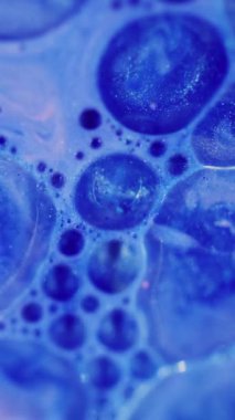 Dikey video. Parlayan kabarcıklar. Odaklanmamış ıslak damla. Yanıp sönen parlak parlak parlak mavi renkli yağ sıvısı soyut modern arkaplanda hareket ediyor..