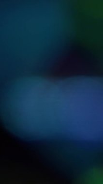 Dikey video. Soyut işaret fişeği. Bulanık renkli parıltı. Odaklanmamış mavi yeşil lens dokusu. Sanatın koyu siyah arka planında ışık yanıp sönüyor..