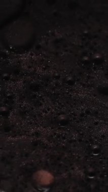 Dikey video. Köpük sıvısı. Yağ sıvısı dokusu. Suyun içindeki koyu siyah bronz boya soyut sanat arka planına yayılıyor..
