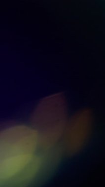 Dikey video. Optik renk. Bulanık soyut ışık. Odaklanamayan sarı gökkuşağı spektrumu aydınlatma deseni koyu siyah arkaplanda parıldıyor..