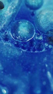 Dikey video. Parlak kabarcıklar. Odaklanmamış parlaklık rengi. Mavi yanıp sönen parlak boya sıvısı soyut bulanık bokeh ışığı modern arka planda hareket ediyor.