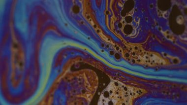 Dikey video. Kimyasal sıvı. Damlacıklar akar. Odaklanmamış sarı mor renkli mürekkep sıvısı. Soyut arkaplanda yüzen bronz mavi pembe..