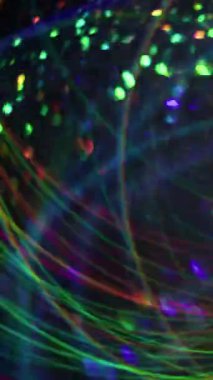 Dikey video. Kaleydoskop yansıması. Odaklanamayan şenlik titreşimleri. Bulanık bokeh ışık arka planında hareket eden çok renkli parçacıkların parlamaları.