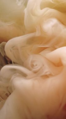 Dikey video. Su altı patlaması. Boya suyu sıçraması. Odaklanmamış sarı turuncu duman dokusu soyut sanat arka planına yayılıyor..