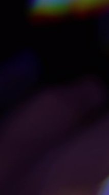 Dikey video. Gökkuşağı yansıması. Bulanık ışık. Odaklanmamış mavi, yeşil, parlak ışık spektrumu soyut koyu siyah arkaplanda titreşiyor..
