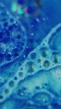 Dikey video. Köpüklü köpük. Odaklanamayan parlak parıltı. Yağ dokusu yaratıcı mavi renk mürekkebi soyut bulanık bokeh ışık arkaplanı üzerinde sıvı akışını sağlar.