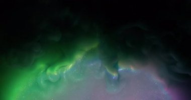 Mürekkep sıçraması. Parlak parçacıklar. Odaklanmamış yeşil mor renkli simli gökkuşağı parlayan bulut soyut koyu siyah arka planda yayılıyor.