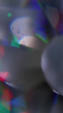 Dikey video. Gökkuşağı topu ışığı. Bulanık parıltı dokusu. Odaklanmamış yeşil kırmızı çok renkli mercek parlaklığı soyut arkaplanda yanıp sönüyor.
