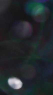 Dikey video. Bulanık parlak bir ışık. Parlak lens. Parlayan parlak parlak çelenk parlak gölgeler çok renkli bokeh açık renk siyah arka planda daireler çiziyor..