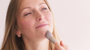 Yüz pudrası. Dekoratif kozmetik. Kozmetik fırça kullanan tatmin olmuş kadın beyaz tenli kadın yüzüne yüz sürüyor..