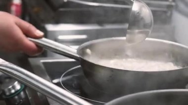 Yemek hazırlıyorum. Acı sos. Aşçı tavaya kepçe suyu ekliyor. Lokanta mutfağında kaynayan gurme yemekleri..