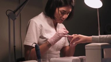 Profesyonel manikür prosedürü. El tedavisi. Manikürcü kız, katı keratini güçlendirmek için oje sürüyor. Yapışkan tabakayı pamuk pedi ile örtüden temizliyor..