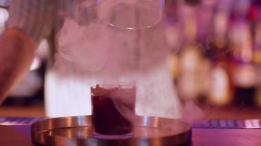 Barmen işi. İçki sunumu. Erkek barmen dumanlı kırmızı alkollü kokteylden cam kaput kaldırıyor. Güzel bir buhar barı tekniği..