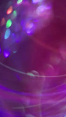 Dikey video. Konfeti parlıyor. Bulanık renkli ışık. Bokeh soyut arka planında yüzen yeşil mor kaleydoskop yuvarlak lens fişeği.