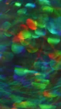 Dikey video. Bulanık renk kıvılcımları. Parıldayan mercek parlıyor. Açık mavi kırmızı yeşil kaleydoskop koyu arkaplanda bokeh ile parlıyor..