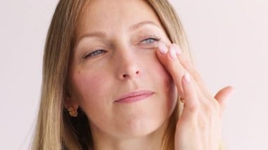 Cilt nemlendirici. Yüz bakımı. Rahatlamış bir kadın beyaza izole edilmiş yaşlanma önleyici krem sürerek yüzüyle ilgileniyor..