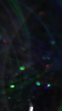 Dikey video. Noel çelengi. Bulanık kıvılcımlar. Lens, koyu siyah bokeh açık sanat arka planında yüzen çok renkli gölgeler oluşturur.