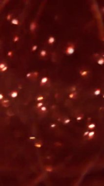 Dikey video. Bulanık parıltı. Bokeh daireleri. Odaklanamayan parlak kırmızı renkli çelenk parıltısı soyut arkaplanda uçuşan kıvılcımlar..