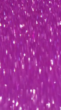 Dikey video. İşaret fişeği. Odaklanamayan parıltı. Pembe eflatun üzerinde parlak bir pırıltı süzülüyor Bokeh ışıltısı ile pembe bir arka plan.