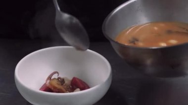 Asya tarifi hazırlanıyor. Deniz ürünleri çorbası. Şefin eli taze domatesli kaşık tüten sıvıyı kaseye dolduruyor. İştah açıcı ahtapot istiridye pişirir..