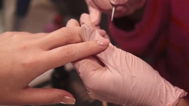 Jel tırnaklar. Profesyonel manikür prosedürü. Kadın eli eldivenli, güzellik salonundaki güzellik teknisyeninin akrilik cilasıyla kapak tedavisi görüyor..