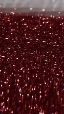 Dikey video. Bulanık parıltı. Altın parçacıkları. Sarı parıltı kırmızı sıvıda yüzüyor Bokeh ışık ışınları arka planda kavisli .