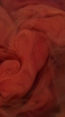 Dikey video. Mürekkebi karıştır. Duman suyu. Odaklanmamış pembe turuncu renkli duman boyası kimyasal madde soyut ruhani akrilik arka planda yüzüyor..