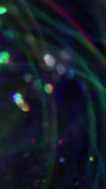 Dikey video. Bulanık çelenk. Parlak arkaplan. Görkemli parlak girdap çok renkli mercek parçacıkları koyu siyah Bokeh ışığı üzerinde parlıyor .