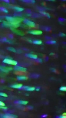 Dikey video. Bulanık kıvılcımlar. Renkli titreşimler. Işıldayan yeşil mavi kaleydoskop mercek fişeği soyut ışık arka planına yayılıyor.