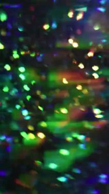 Dikey video. Noel ışıkları. Odaklanamayan havai fişekler. Yeşil mor çok renkli titreşimli kaleydoskop mercekleri bulanık arka planda parlıyor..