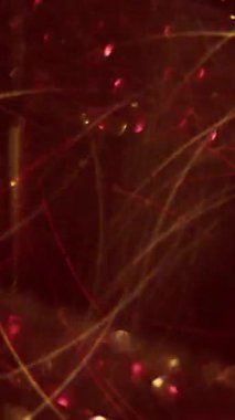 Dikey video. Görüntü pırıl pırıl. Yuvarlak titreşim. Sanatsal renkli ışıltı, kırmızı altın soyut zemin üzerinde parıldayan parçacıklar etrafında parıldıyor..