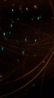 Dikey video. Bulanık konfeti parlıyor. Dönüp duruyor. Soyut parlak optik sarı çizgiler koyu siyah sanat arka planında kırmızı mavi altın rengi açıyor.