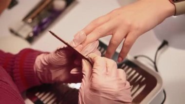 Çivi prosedürü. Salon tedavisi. Manikür ustası kadın elleriyle akrilik tırnak törpülüyor profesyonel mercimek tahtası ile kız müşteri kaplıcası için güzellik yapıyor..