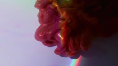 Parıltı akışı. Işıldayan sıvı. Pembe kırmızı duman renkli toz mürekkebi menekşe ışınının soyut arka planına dökülmüş. Su, parlak gökkuşağını çözdü..
