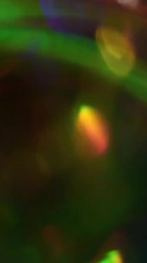 Dikey video. Bulanık kıvılcımlar. Bokeh ışığı. Parıldayan yeşil turuncu mavi renk deseni soyut koyu siyah arkaplanda kıvrılıyor..