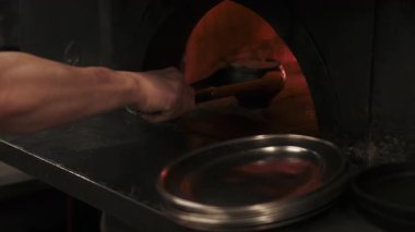 Kızartma işlemi. Ateş fırını pişiyor. Şefin elleri, metal mutfak maşasıyla siyah, sıcak dökme demir yiyeceği çıkarıyor. Geleneksel taze kazan tabağı.