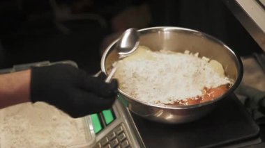 Fırın iş akışı. Mutfak pulları. Eldivenli eller, yumurtalı metal kaseye beyaz kaşık unu ekliyor. Şef hamur tarifi malzemelerini tartıyor..