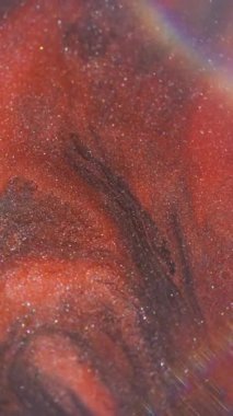 Dikey video. Parlak karışım. Bulanık boya suyu. Odaklanamayan pırlanta ışıkta turuncu, siyah, ışıl ışıl sıvı akış. Girdap rengi soyut arkaplan.