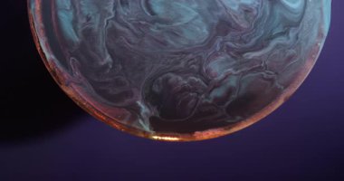 Akrilik bulanıklık dökülüyor. Gezegen renk tutulması. Siyah mavi boya soyut olarak parlayan kemerin etrafında karışıyor. Mor arkaplanda çözünen parıldayan pigment.