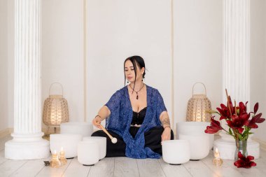 Kristal müzik kaseleri. Kadın meditasyonu. Ses terapisinin keyfini çıkaran kadın, kapalı alanda tedavi için buhar ateşi mumları yakıyor..