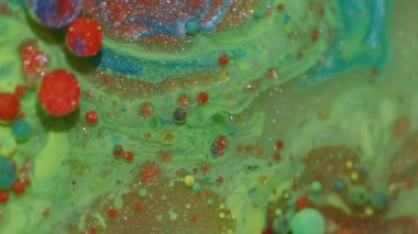 Canlı bir sıvı. Renk sıvısı. Odaklanmamış yeşil mavi parlak mürekkep köpükleri soyut arkaplanda parlayan turuncu pigmentler..