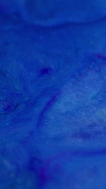 Dikey video. Dalga sanatı. Mürekkep sıvısı. Odaklanmamış mavi renkli su damlacıkları soyut ve canlı arkaplanda yüzen ışıltılı sıçrama dokusu.